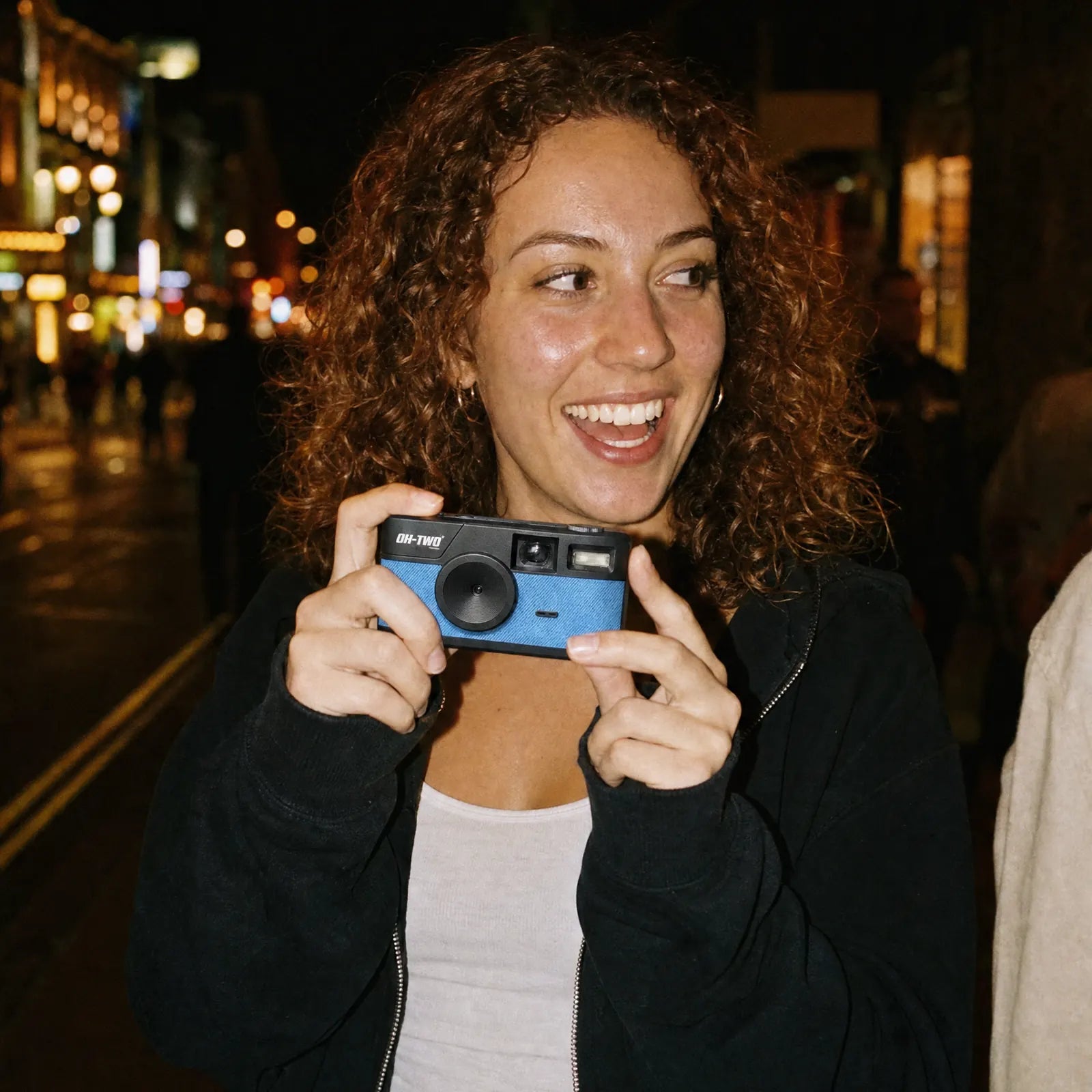 A woman holding the pocket-sized OH—TWO Digital Film camera on a night out