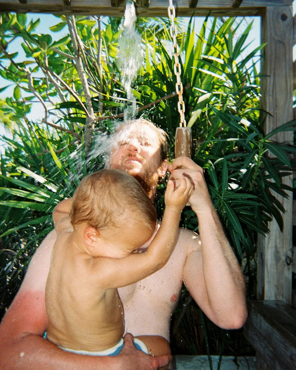 A dad and his baby laughing under an outdoor shower